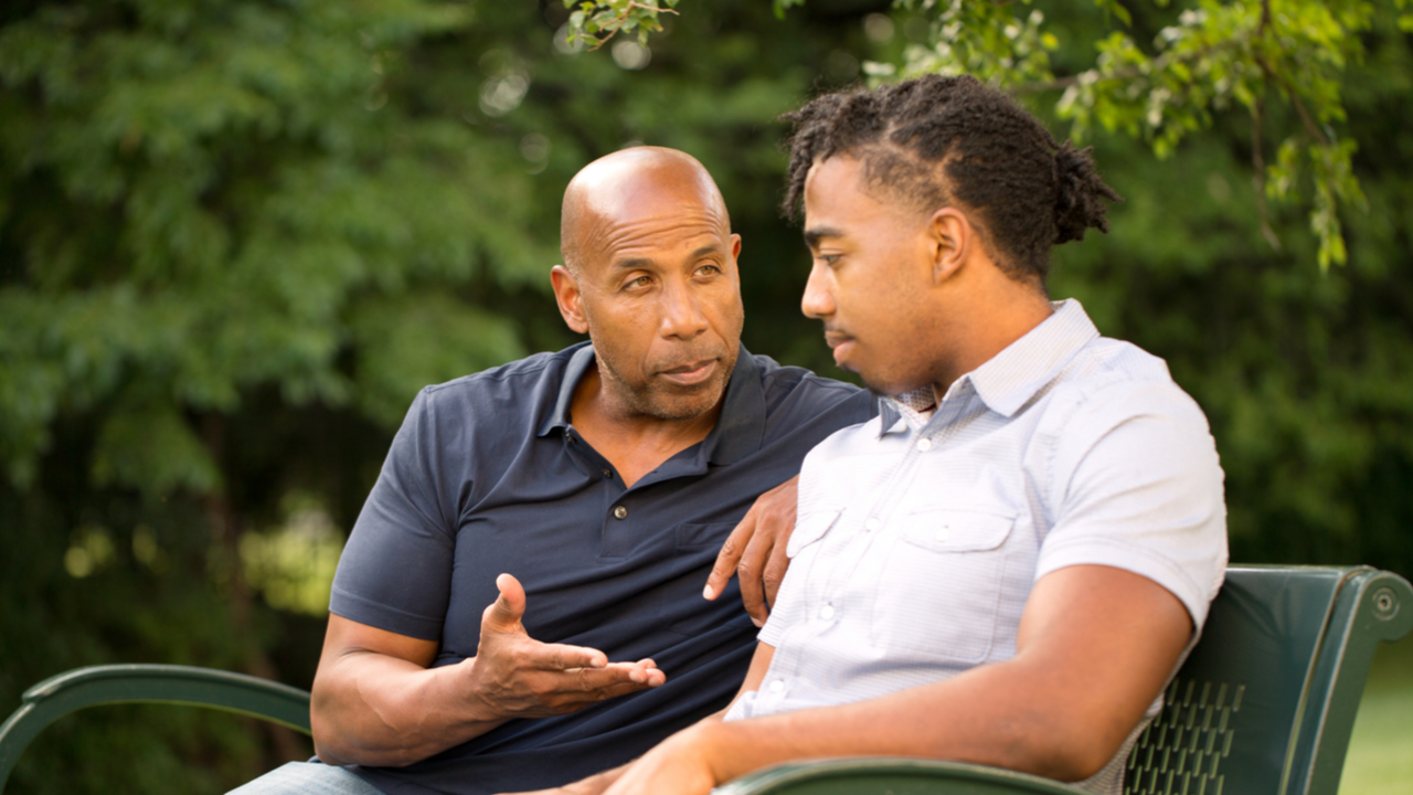 Male mentor and male mentee sitting outside in a park