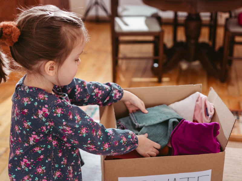 To help her family with spring cleaning, a child places old clothes in a box to be donated.